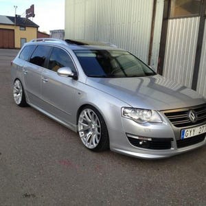 Może przedstawiać: Srebrne kombi Volkswagen Passat z obniżonym zawieszeniem, niestandardowymi wieloramiennymi felgami aluminiowymi, przyciemnianymi szybami i szyberdachem. Pojazd posiada szwedzką tablicę rejestracyjną o treści GYY 277 na przednim zderzaku.