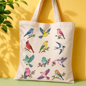 May include: A cream-colored canvas tote bag featuring a grid of twelve colorful illustrations of various birds, including blue, yellow, red, and pink species perched on branches or in flight, with two sturdy shoulder straps at the top.