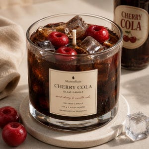 Peut inclure: Une bougie en verre remplie de cire brun foncé ressemblant à du cola à la cerise, surmontée de glaçons transparents et de cerises rouges. L'étiquette indique MaisonRain CHERRY COLA, sweet cherry & vanilla cola, SOY WAX CANDLE, 220 g, 45-50 HOURS, HANDMADE IN SARAJEVO.