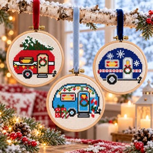 Op de afbeelding: Drie ronde houten borduurringen met kruissteekontwerpen van vintage campers. Een rode camper met een boom, een blauwe met cadeaus en een donkerblauwe met sneeuwvlokken, elk opgehangen aan een gekleurd fluwelen lint.