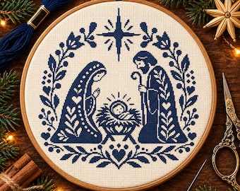 Op de afbeelding: Een ronde houten borduurring met een kruissteekpatroon op crèmekleurige stof. Het ontwerp toont een donkerblauwe kerststalscène met een centrale ster, omringd door een decoratieve krans van bladeren, hartjes en bloemmotieven.