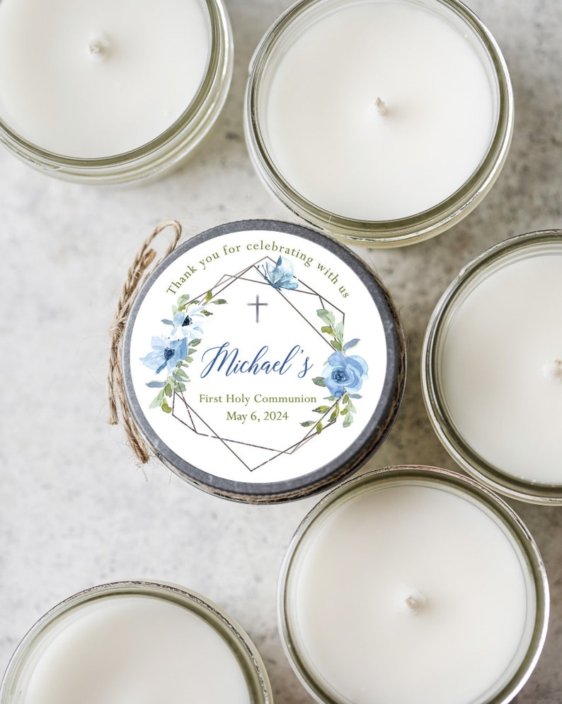 May include: A set of four small glass jars with white candles. Each jar has a round label with a blue and green floral design, a gold geometric frame, and the text "Thank you for celebrating with us + Michael's First Holy Communion May 6, 2024".