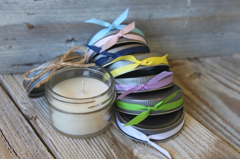 May include: A stack of small glass jars with metal lids, each tied with a different colored ribbon. The jars are filled with white candle wax and have a single wick.