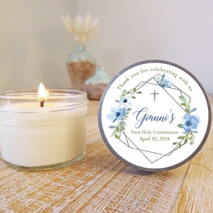May include: A white candle in a clear glass jar with a blue and green floral design label. The label says "Thank you for celebrating with us" and "Gianni's First Holy Communion April 30, 2024".