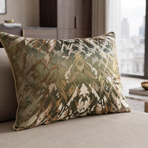 May include: A rectangular throw pillow featuring an abstract, multi-tonal pattern in shades of olive green, tan, and cream. The fabric has a subtle sheen and is finished with a decorative twisted cord trim along the edges, creating a textured border.