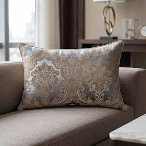 Peut inclure: Un coussin rectangulaire orné d'un motif damassé bleu clair et or métallique. Le tissu présente une texture tissée avec des volutes et des motifs floraux complexes. Les bords du coussin sont finis avec un fin passepoil doré assorti.