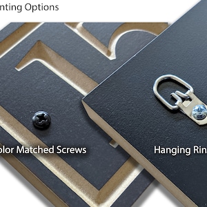 Puede incluir: Primer plano de dos paneles de madera negros con herrajes de montaje. Un panel presenta un tornillo del mismo color, y el otro tiene un anillo para colgar. El texto "Opciones de montaje" est&aacute; en la parte superior, y "Tornillos del mismo color" y "Anillos para colgar" est&aacute;n etiquetados.