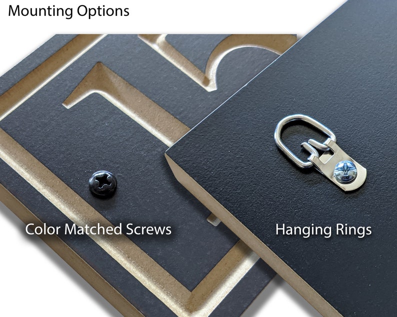 Puede incluir: Primer plano de dos paneles de madera negros con herrajes de montaje. Un panel presenta un tornillo del mismo color, y el otro tiene un anillo para colgar. El texto "Opciones de montaje" est&aacute; en la parte superior, y "Tornillos del mismo color" y "Anillos para colgar" est&aacute;n etiquetados.