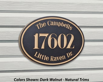 Puede incluir: Placa de dirección ovalada en nogal oscuro con borde natural, con "The Campbells", el número "17602" y "Little Raven Dr.". Montada sobre revestimiento gris claro.