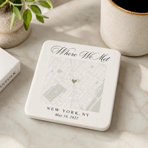 Peut inclure: Un dessous de verre carré en pierre blanche avec une carte imprimée de New York, NY. Le texte "Where We Met" figure en haut, avec une petite icône de cœur sur la carte. Le bas indique "NEW YORK, NY" et la date "May 18, 2022" en noir.