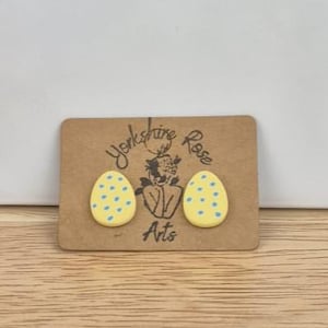 May include: A pair of yellow egg-shaped earrings with blue polka dots. The earrings are on a brown card with the text "Yorkshire Rose Arts".