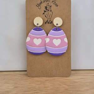 Könnte beinhalten: Lila und rosa eiförmige Ohrringe mit weißen Herzen. Die Ohrringe befinden sich auf einer braunen Karte mit dem Text "Yorkshire Rose Arts".