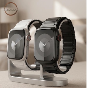 May include: Two smartwatches displayed on a metallic stand. One watch features a white case and matching link band, while the other has a black case and matching link band. Both devices have dark screens with a circular graphic and a side crown.