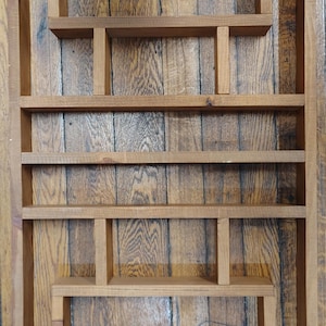 May include: A rectangular wooden wall shelf featuring a medium brown finish and a natural wood grain texture. The unit is constructed with a series of fixed horizontal and vertical dividers, creating multiple open compartments of varying sizes.
