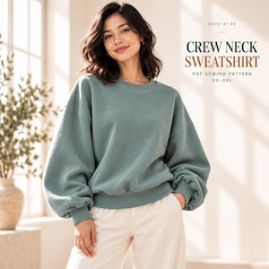 Könnte beinhalten: Ein salbeigrünes Sweatshirt mit Rundhalsausschnitt, langen, voluminösen Ärmeln und gerippten Bündchen. Der Text auf dem Bild lautet: GHOST BY OK, CREW NECK SWEATSHIRT, PDF SEWING PATTERN, XS-3XL. Das Sweatshirt wird mit einer hellen Hose kombiniert.