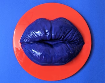 May include: A bright red circle with a glossy, dark blue, three-dimensional sculpted lip sculpture in the centre.