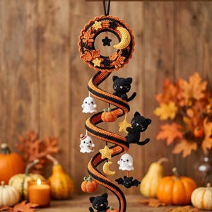 May include: A hanging crochet spiral decoration featuring black and orange stripes. It is adorned with small crocheted figures including black cats, white ghosts, orange pumpkins, yellow stars, a yellow crescent moon, and a black bat.