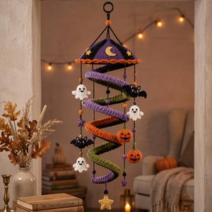 May include: A hanging spiral crochet mobile featuring a purple, orange, and green coiled structure. It is decorated with small crocheted figures including white ghosts, black bats, and orange jack-o'-lanterns, accented with purple and yellow stars.