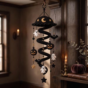 May include: A hanging crochet mobile featuring a central black spiral structure decorated with small white ghosts, black bats, orange jack-o'-lanterns, and yellow stars. The top dome is black with a yellow crescent moon and star accents.