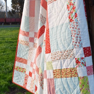 May include: A white, red, and green patchwork quilt with a light blue backing. The quilt is quilted with a curved design.