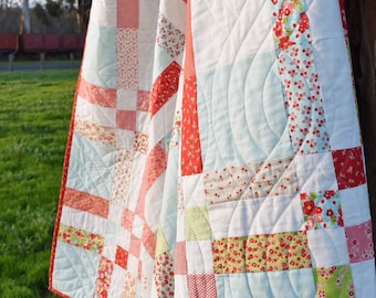 May include: A white, red and green patchwork quilt with a light blue backing. The quilt is quilted with a curved design.