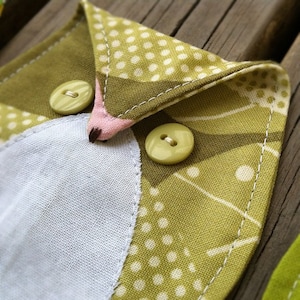 May include: A green fabric owl with white polka dots and a white fabric belly. The owl has two yellow buttons for eyes.