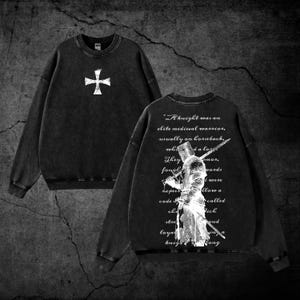 May include: A black crewneck sweatshirt featuring a white cross graphic on the front. The back displays a white illustration of a knight holding a sword, overlaid with the text: A knight was an elite medieval warrior, usually on horseback.