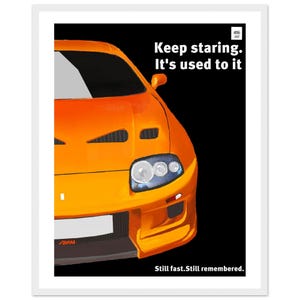 Peut inclure: Une affiche présentant la vue avant d'une voiture de sport orange sur un fond noir. Le texte indique "Keep staring. It's used to it" et "Still fast. Still remembered.". La voiture possède un phare proéminent, une calandre et un logo Supra.