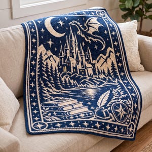 May include: A navy blue and cream crochet blanket featuring a detailed scene of a castle, a flying dragon, a crescent moon, stars, a stack of books, and an inkwell with a quill, all enclosed within a decorative star-patterned border.