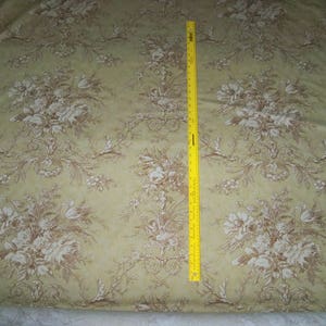 Puede incluir: Un primer plano de una tela beige con un patr&oacute;n floral marr&oacute;n. La tela est&aacute; doblada y una cinta m&eacute;trica amarilla es visible en el lado derecho de la imagen.