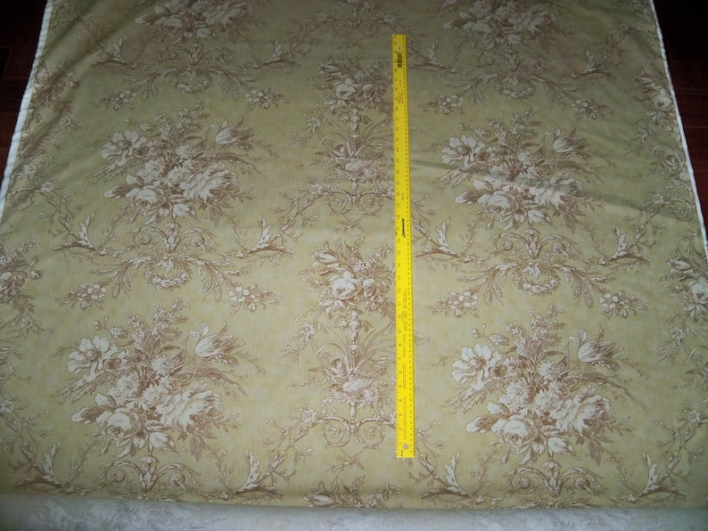 Puede incluir: Un primer plano de una tela beige con un patr&oacute;n floral marr&oacute;n. La tela est&aacute; doblada y una cinta m&eacute;trica amarilla es visible en el lado derecho de la imagen.