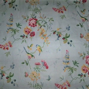 Könnte beinhalten: Ein hellblauer Stoff mit einem floralen Muster mit rosa, gelben und weißen Rosen, blauen und gelben Vögeln und Schmetterlingen. Der Hintergrund ist hellblau.