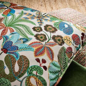 May include: A white pillow with a colorful embroidered floral pattern. The design features a variety of flowers, leaves, and vines in shades of blue, green, red, yellow, and brown.