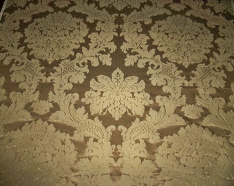 Può includere: Primo piano di un tessuto marrone con un motivo damascato dorato. Il tessuto ha una leggera lucentezza e una texture in rilievo.