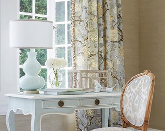 May include: A light blue desk with two drawers, a white lamp, and a floral curtain. A decorative birdcage and a vase of white flowers sit on the desk. A wooden chair with patterned fabric is next to the desk.