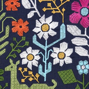 Pode incluir: Close-up de um tecido azul marinho com bordado floral colorido. O design apresenta margaridas brancas com centros amarelos, flores laranja e rosa e elementos vegetais estilizados verdes e azuis.