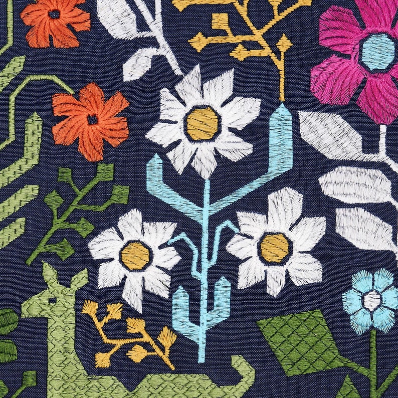 Pode incluir: Close-up de um tecido azul marinho com bordado floral colorido. O design apresenta margaridas brancas com centros amarelos, flores laranja e rosa e elementos vegetais estilizados verdes e azuis.