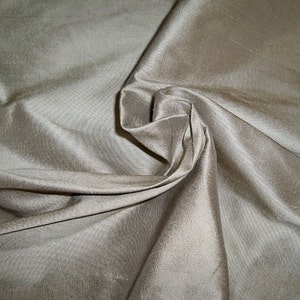 May include: A close-up of a smooth, silky fabric in a light beige colour. The fabric is draped and folded, showcasing its texture and drape.