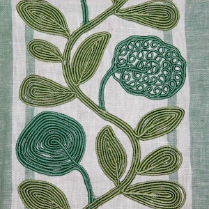 Può includere: Un tessuto verde chiaro con un pannello verticale centrale bianco con ricamo a cordoncino verde scuro e verde chiaro. Il ricamo raffigura una vite sinuosa con foglie ovali e due forme floreali circolari realizzate con cordoncino verde.