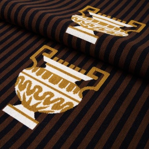 May include: A brown and black striped fabric with a white and gold embroidered design of two urns. The urns have a Greek key design and are facing opposite directions.