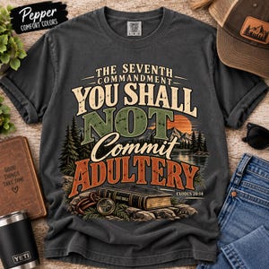 Puede incluir: Una camiseta gris carbón con un estampado gráfico que incluye el texto THE SEVENTH COMMANDMENT YOU SHALL NOT COMMIT ADULTERY EXODUS 20:14. El diseño muestra un paisaje con montañas, un lago, una puesta de sol, una Biblia y una brújula.