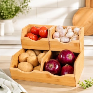 May include: A two-tiered bamboo storage bin organizer featuring four open compartments. The top left bin holds red tomatoes, the top right holds white garlic bulbs, the bottom left contains brown potatoes, and the bottom right holds red onions.