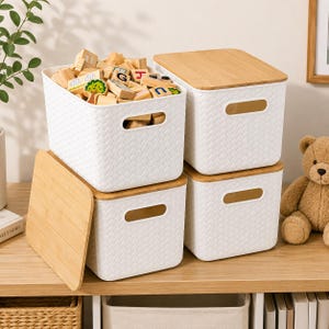 May include: Four rectangular white storage bins with a woven texture and integrated handles. Two bins have light brown wooden lids placed on top, one bin is open and filled with wooden alphabet blocks, and one lid rests on the side.