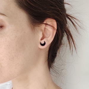 Può includere: Una persona indossa orecchini neri a forma di mezzaluna. Gli orecchini sono realizzati in un materiale nero liscio.