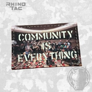 May include: A rectangular patch featuring a photographic print of a large group of people standing in a room with a patterned floor. The text "COMMUNITY IS EVERYTHING" is printed in bold white capital letters across the center of the image.