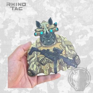 May include: A tactical patch featuring an illustrated rhinoceros wearing tan combat gear and night vision goggles with glowing blue lenses. The rhino holds a black submachine gun. The text RHINO TAC is printed in the upper left corner of the image.