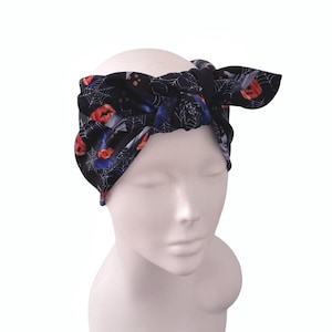Könnte beinhalten: Ein schwarzes Stoffstirnband mit einem wiederkehrenden Halloween-Muster aus orangefarbenen Kürbissen, weißen Spinnennetzen und blauen Akzenten. Das Stirnband hat einen Knoten in der Mitte und wird auf einem weißen Schaufensterpuppenkopf präsentiert.