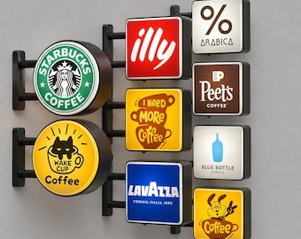 Könnte beinhalten: Ein Wanddisplay mit mehreren beleuchteten Schildern, die verschiedene Kaffeemarken-Logos und Grafiken zeigen, darunter Starbucks, illy, Arabica, Peet's, Blue Bottle, Lavazza sowie individuelle Designs mit Texten wie I Need More Coffee und Wake Cup.