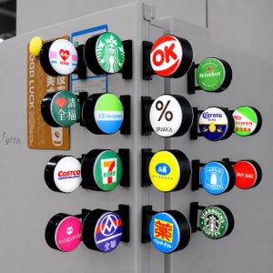 May include: A collection of small, circular, illuminated signs featuring various brand logos including Starbucks, Heineken, Costco, 7-Eleven, FamilyMart, and others. Each sign is mounted on a black bracket attached to a light gray surface.