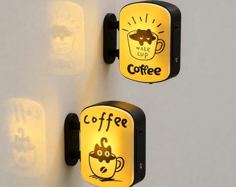 May include: Two wall-mounted, illuminated, rectangular signs with rounded corners. Each sign features a black frame, a yellow glowing face, and a black graphic of a cat inside a coffee cup. The top sign says "WAKE CUP" and "Coffee," while the bottom sign says "coffee."
